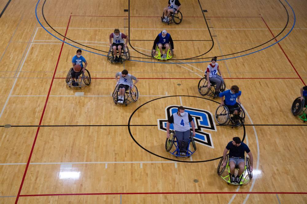 Adults wheeling in wheelchairs during a basketball game.